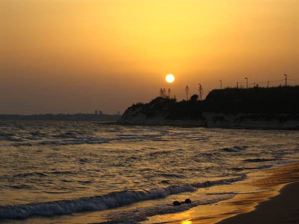 Low sun on the horizon, waves on the sand, backlit cliff with lampposts