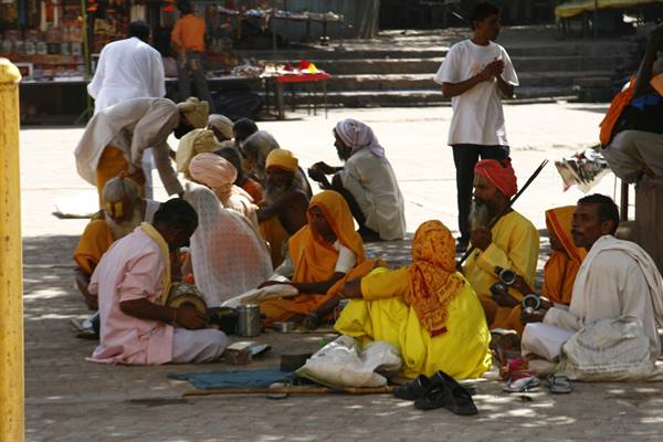 Pilgrims and sadhus in yellow robes sitting in the shade of a square