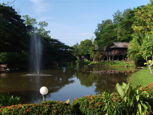 Fountain on pond in front of wooden stilt houses among tropical plants