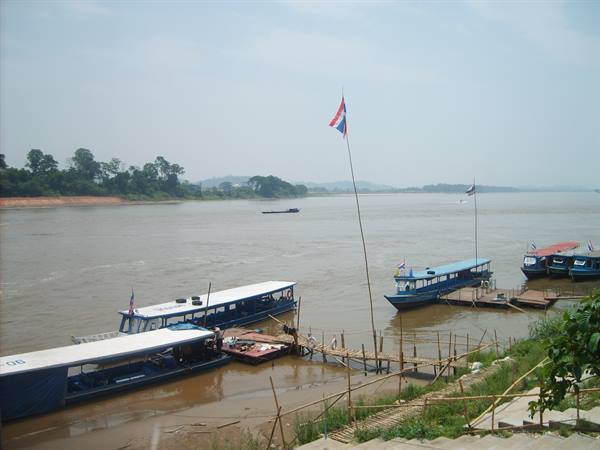 Wooden longtail boats moored on the Mekong river, flags in the wind