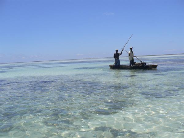 Two fishermen paddling a wooden boat across shallow turquoise water