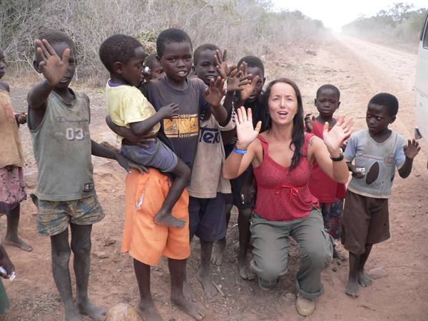 Woman crouching with waving children on a dusty dirt road