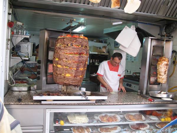 Cook in kitchen slicing a large meat skewer in front of the counter