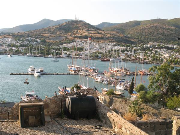 Boats moored in Bodrum harbour seen from the castle, white houses below dry hills
