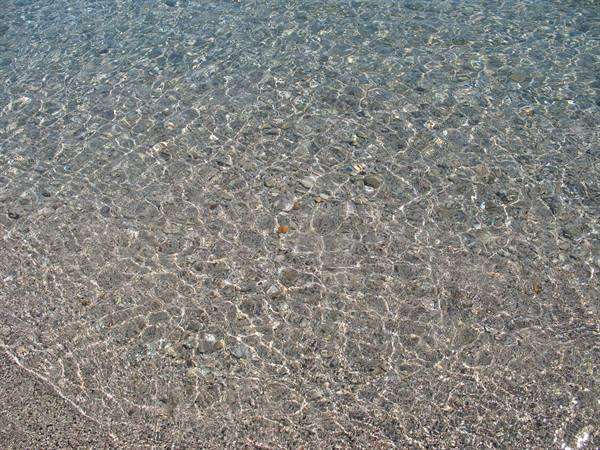 Clear water over grey pebbles, sunlight rippling on the seabed
