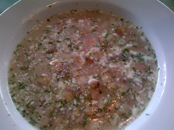Hot soup with herbs, grated cheese and tomato, served in a white bowl
