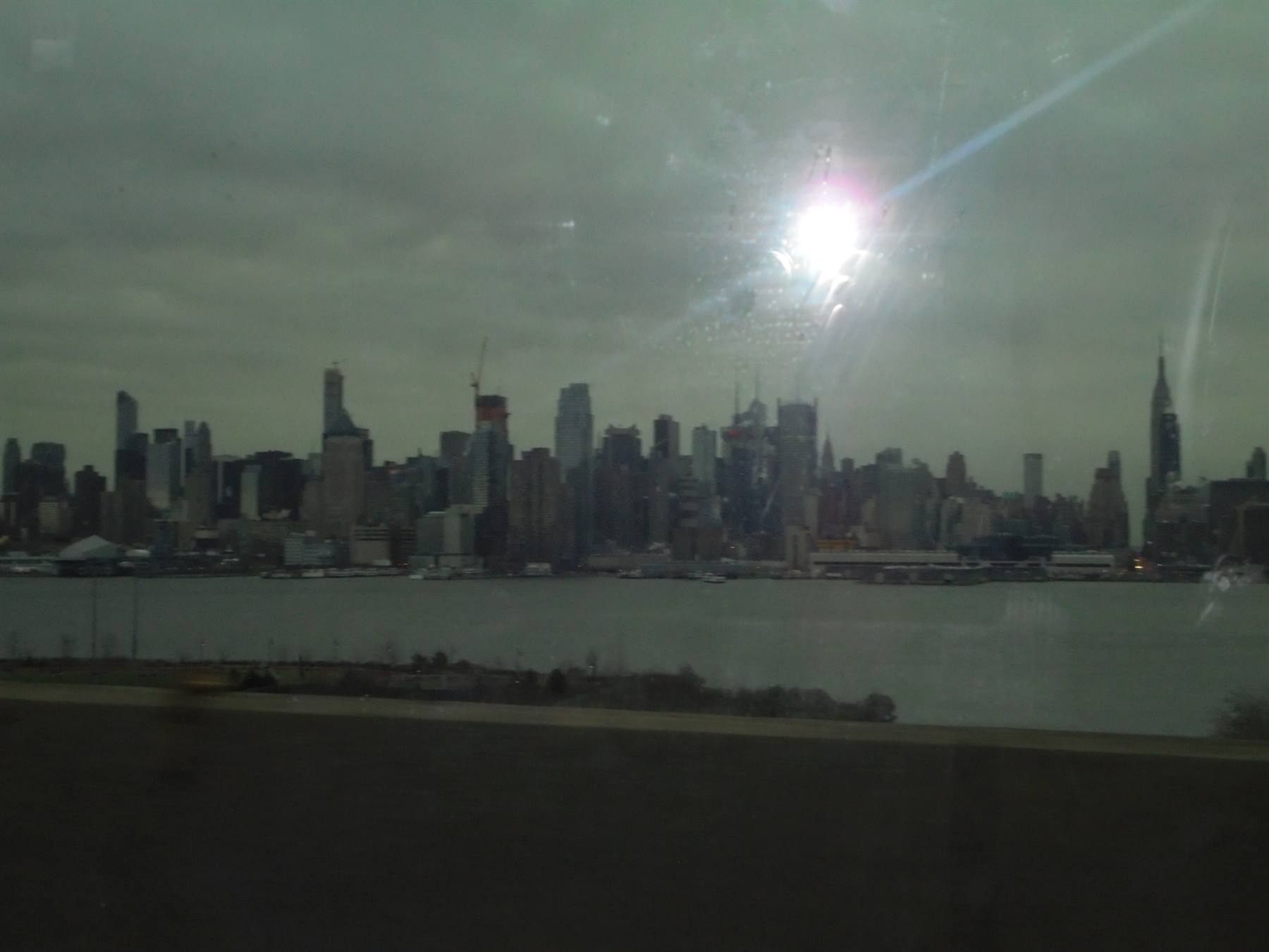 Grattacieli di Manhattan oltre il fiume Hudson, cielo grigio e sole