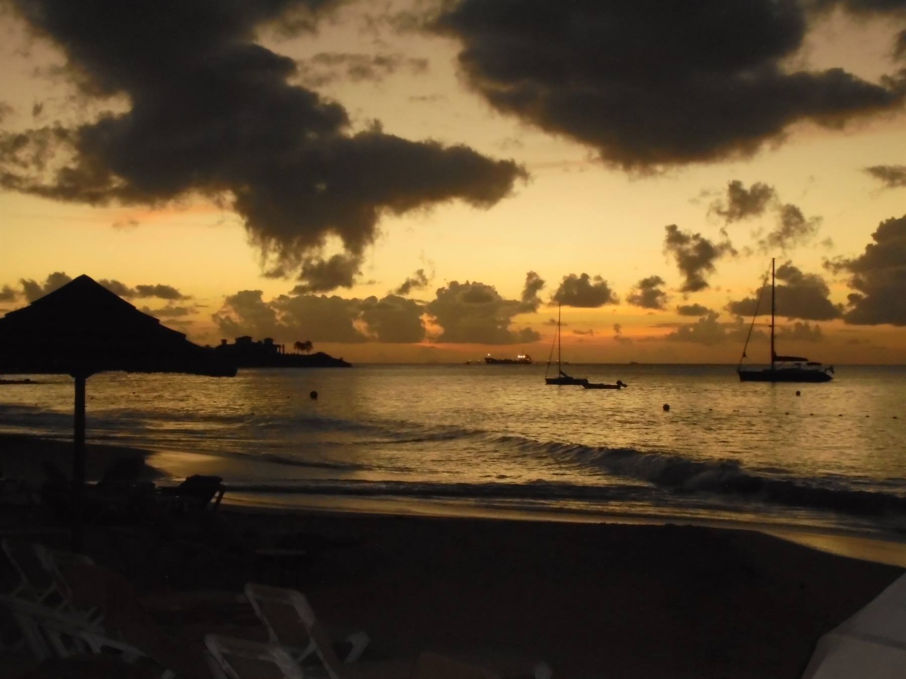 Ombrellone e sdraio in controluce su spiaggia con barche ancorate