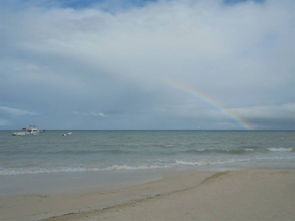 Rainbow over the sea, anchored boats and waves on the sandy beach