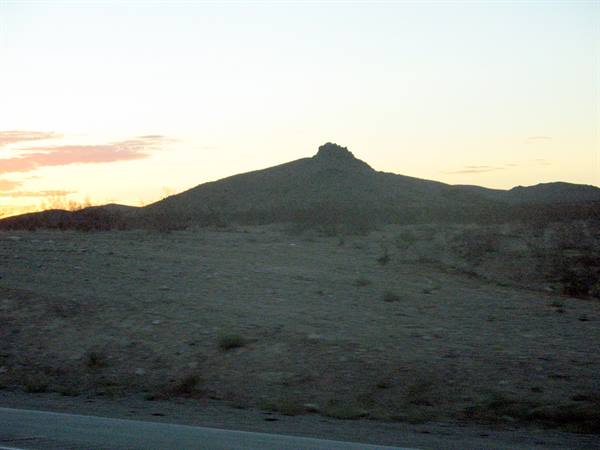 Rocky butte in desert at dusk, scattered shrubs and pale sky