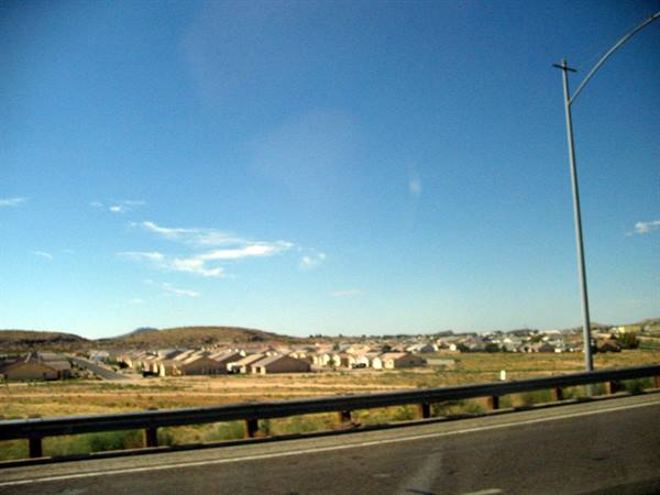 Low desert houses seen from the highway, metal guardrail, blue sky