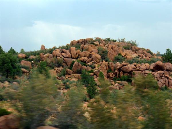Red granite boulders among green shrubs under gray sky, motion blur