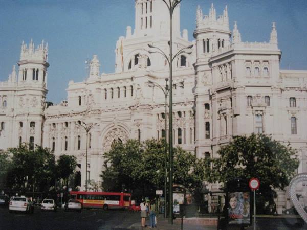 Pedestrians and a bus pass the white Cibeles Palace on a bright Madrid day