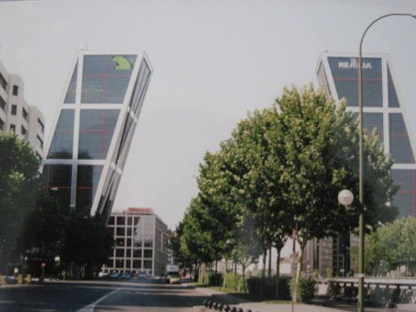 The inclined glass KIO towers rising above trees along the avenue