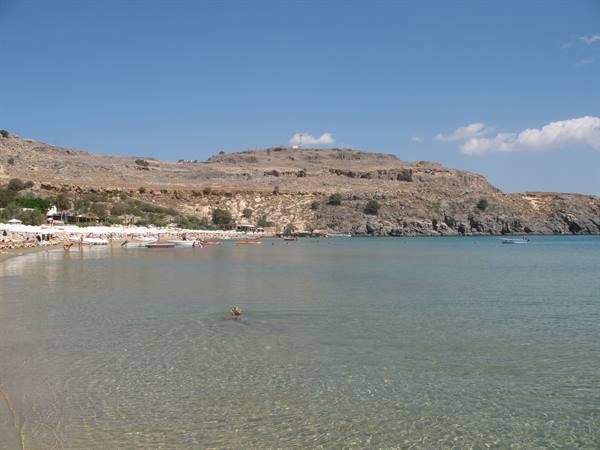 Lindos bay: clear turquoise water, boats and umbrellas beneath the rocky hill