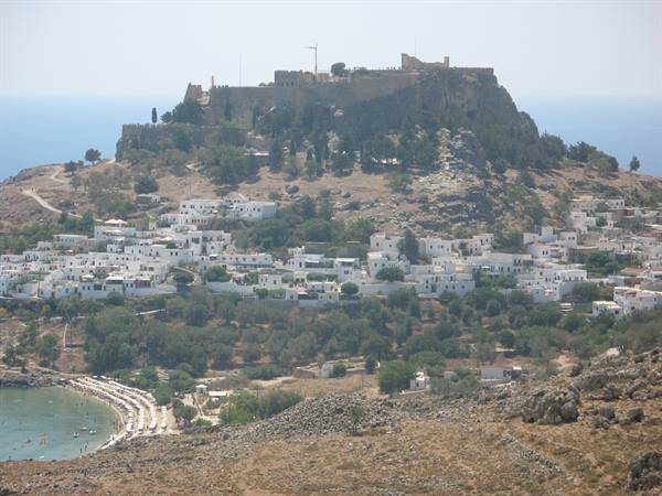 Lindos: white houses beneath the rocky acropolis and beach with umbrellas