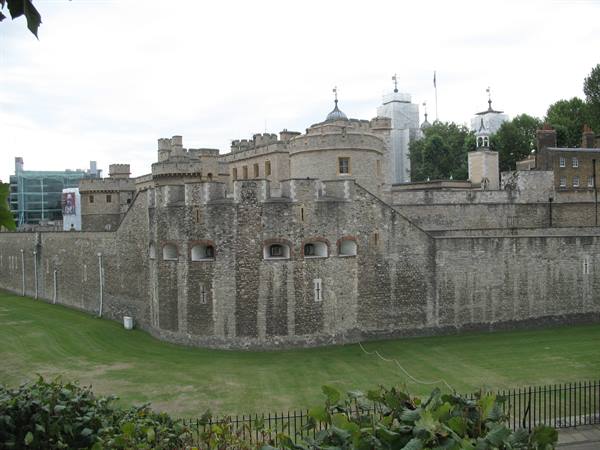Medieval stone walls of the Tower of London, green lawn under overcast sky