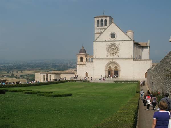 Visitors walk toward the Basilica of Saint Francis in Assisi, green lawn and clear sky