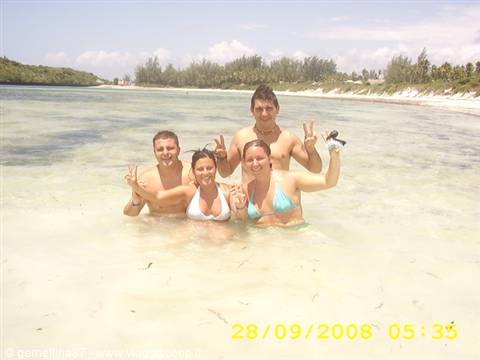 Four friends flash peace signs in clear water on a tropical beach