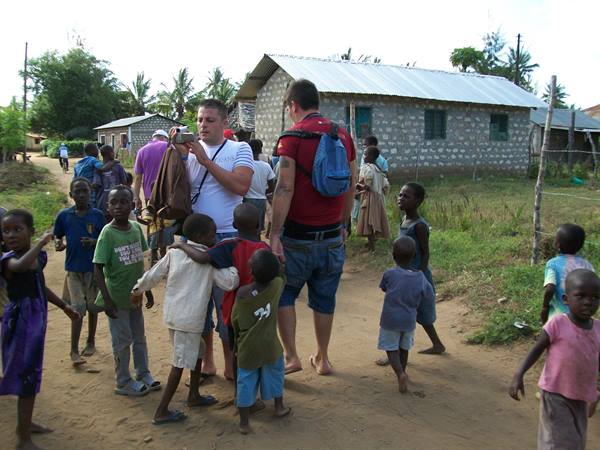 Tourists among local children on a dirt road near concrete block houses