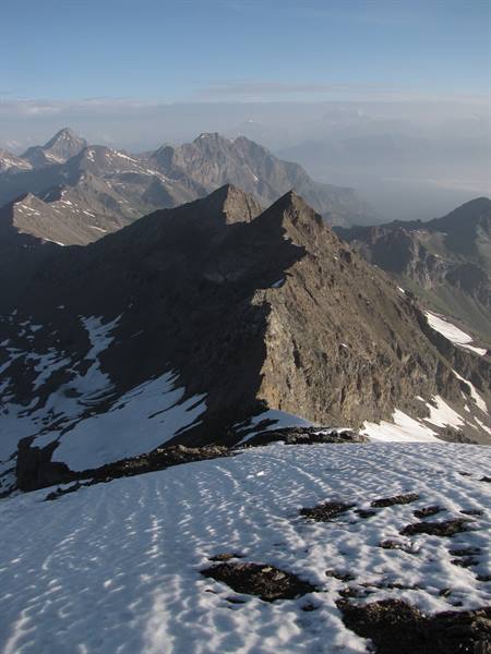 Rocky ridge with snow patches, hazy alpine peaks in morning fog