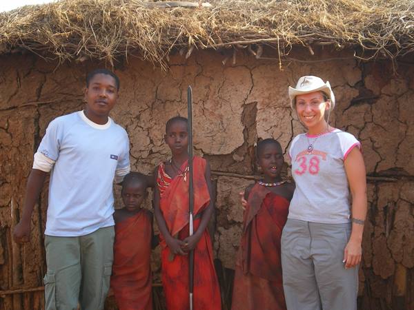Tourist with a Maasai family in front of a mud and thatch hut