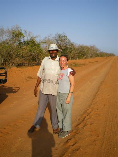 Two people hugging on a red dirt road with bushes and a jeep