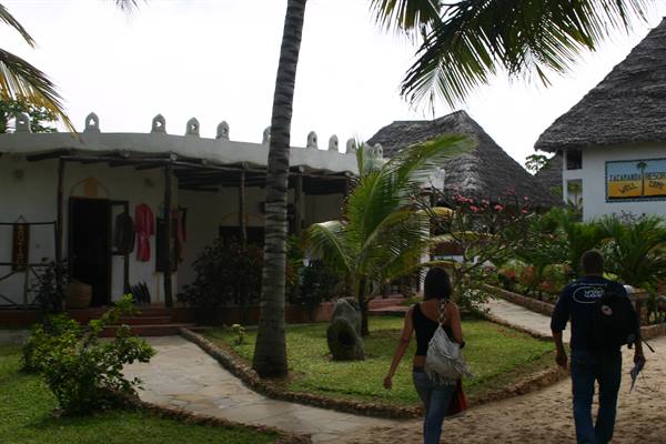 Tourists walk through the garden of a resort with thatched-roof cottages