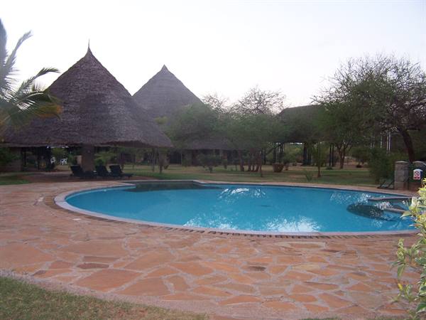 Round swimming pool on stone paving beside thatched-roof huts