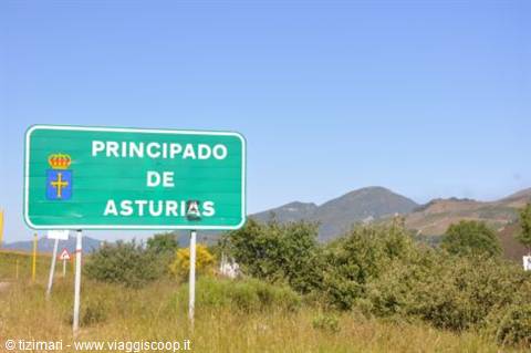 Green road sign marking Principado de Asturias border, hills and bushes behind
