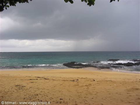 Golden sand beach with black rocks, gray rain clouds overhead