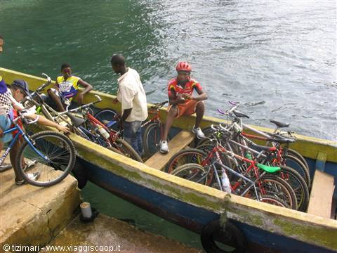 Cyclists loading mountain bikes onto a green wooden boat on turquoise water
