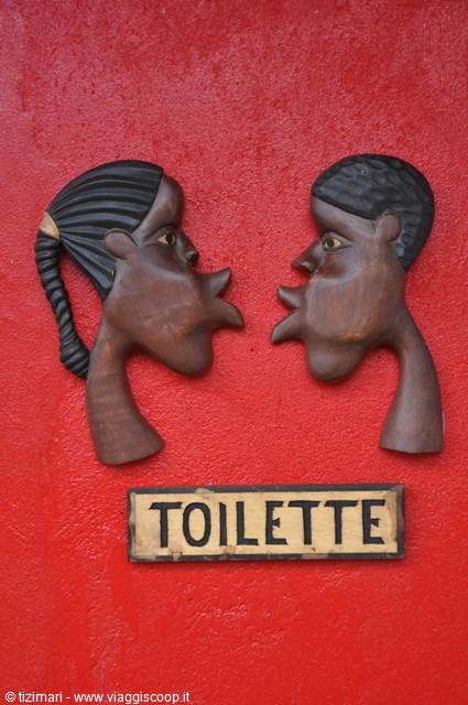 Wooden sign with two carved heads and toilette lettering on red wall