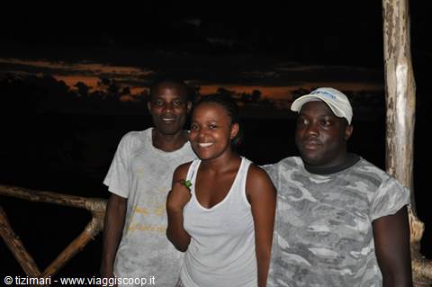 Three friends smiling at night on a wooden terrace by the sea