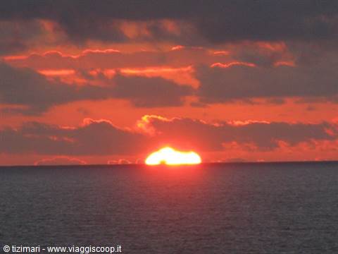 The red sun sinks among clouds over the open sea horizon