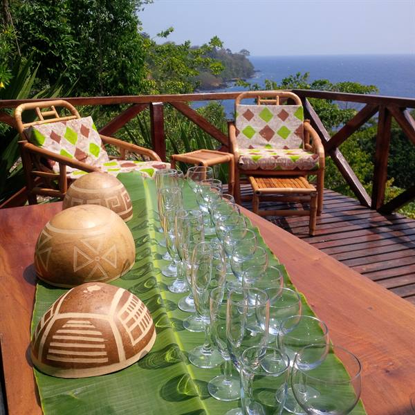 Glasses and carved bowls on banana leaf, wooden terrace overlooking the sea