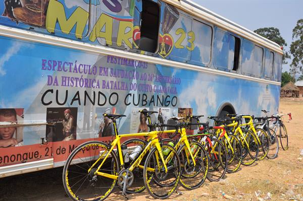 Yellow racing bikes lined up beside a decorated tour bus in Cuando Cubango