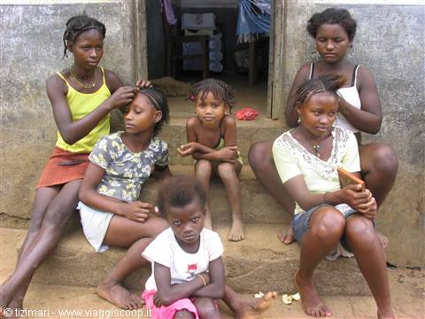 Six young girls sitting on concrete steps outside a house, one braiding another's hair