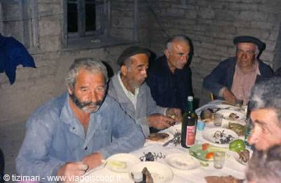 Bearded men sharing food and wine at a table in a brick room