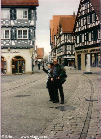 Two people pose on the cobblestone street among German half-timbered houses