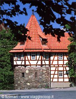 Half-timbered medieval tower with red tiled roof among green trees