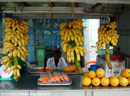 Fruit vendor at stall with hanging bananas and papayas