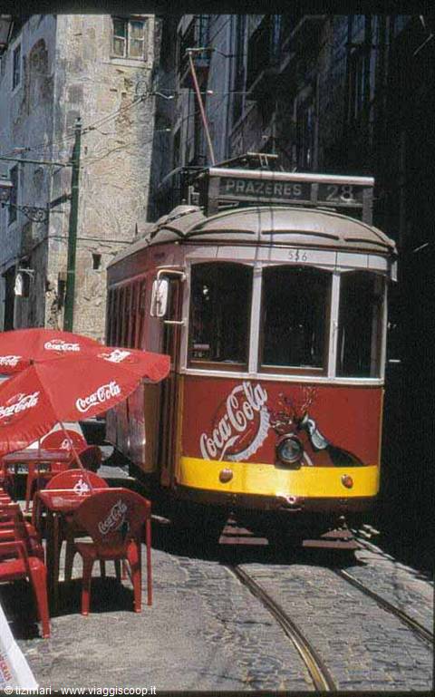 Tram 28 to Prazeres covered in Coca-Cola ads beside red umbrellas, Lisbon