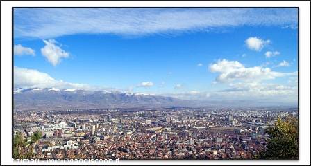 Sprawling city beneath snowy mountains, low houses and towers under blue sky