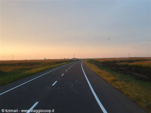 Straight asphalt road through farmland under an orange sky