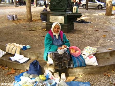 Elderly woman in white headscarf selling socks and goods on square steps