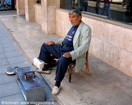 Man sitting on a cane chair shining shoes on the sidewalk