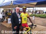 Cyclist in yellow jersey on podium with flowers under a tent