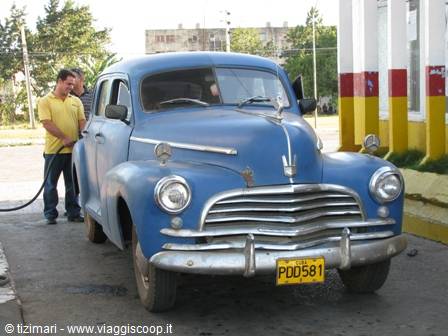 Blue vintage car at gas station, man refueling beside it