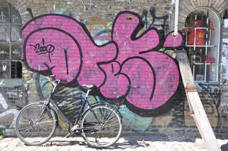 Bicycle leaning against a grey brick wall with pink graffiti